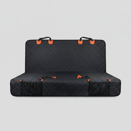 Dog sitting on a black car seat cover with orange straps in a vehicle.