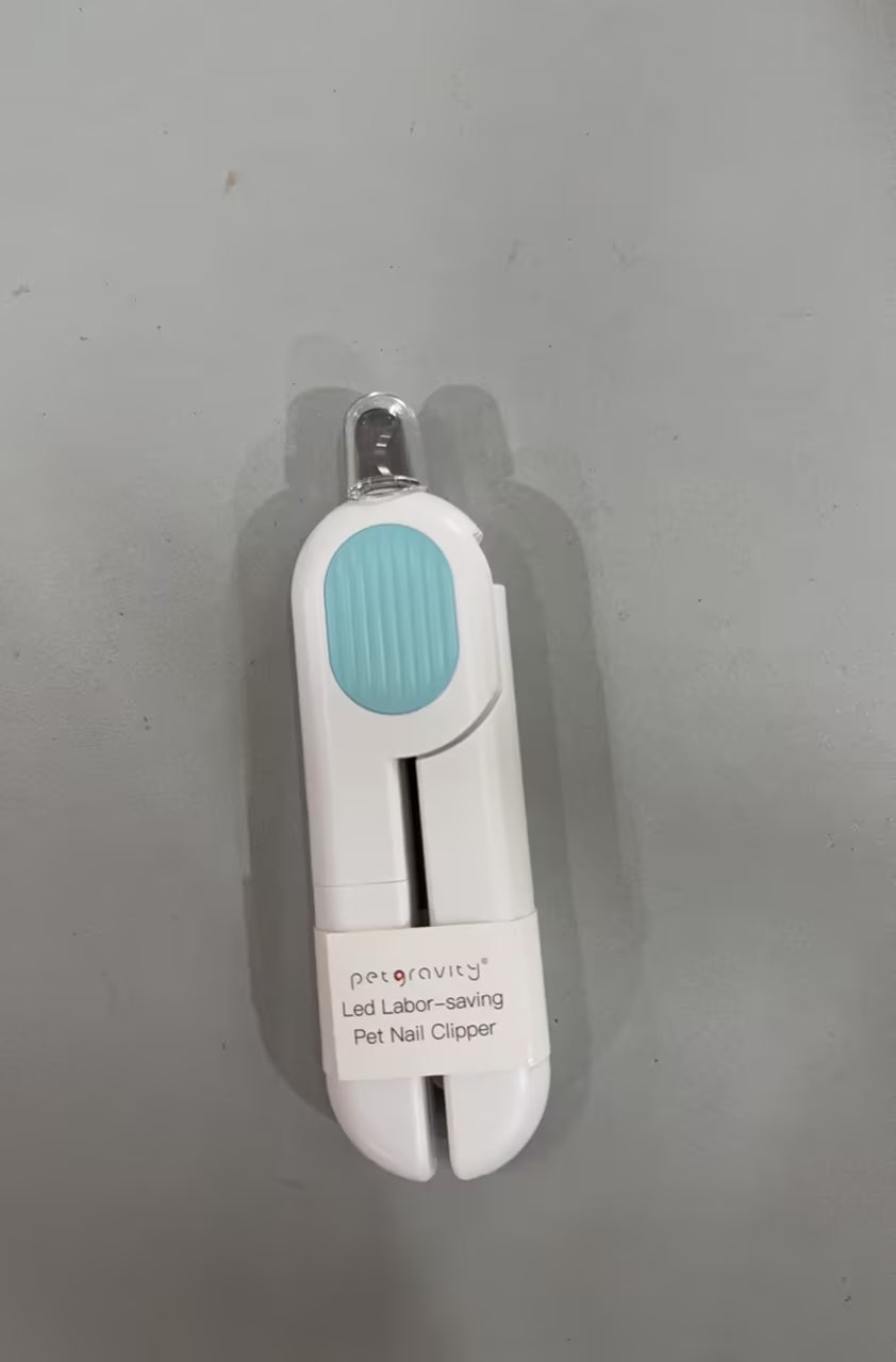 A pet nail clipper tool with a white body, a light blue textured grip, and a clear plastic cap, resting on a gray surface. The label reads 'pergravity Led Labor-saving Pet Nail Clipper'.